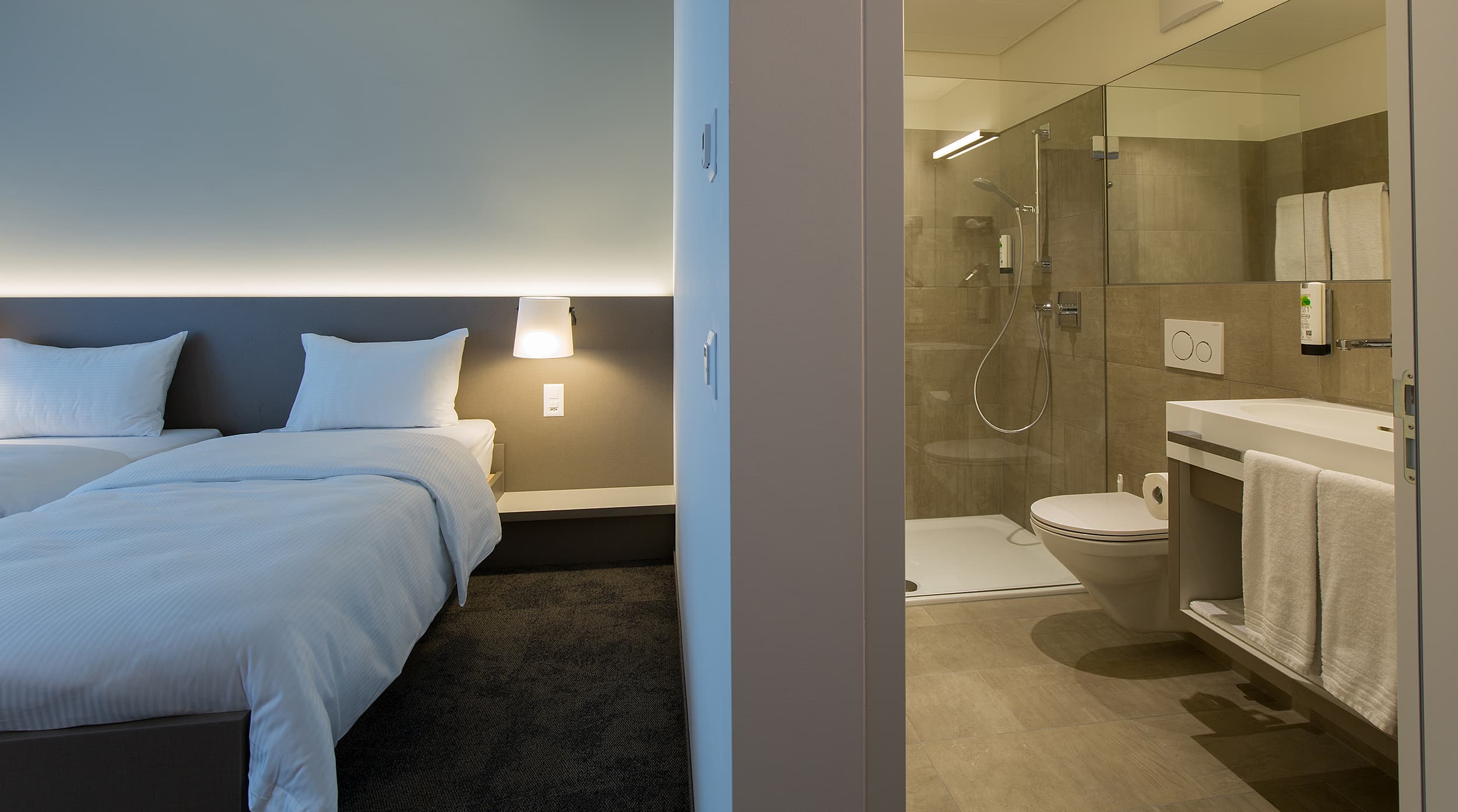 A modern double room at the b_smart motel Landquart with two beds, stylish lighting, and an adjoining bathroom with a shower.