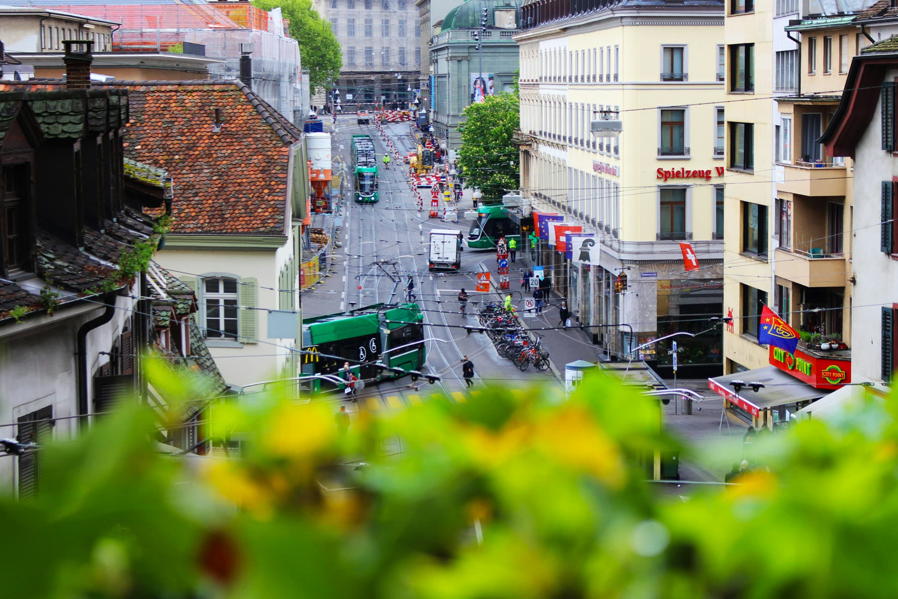 View of a busy street in Basel with streetcars bike racks and surrounding buildings
