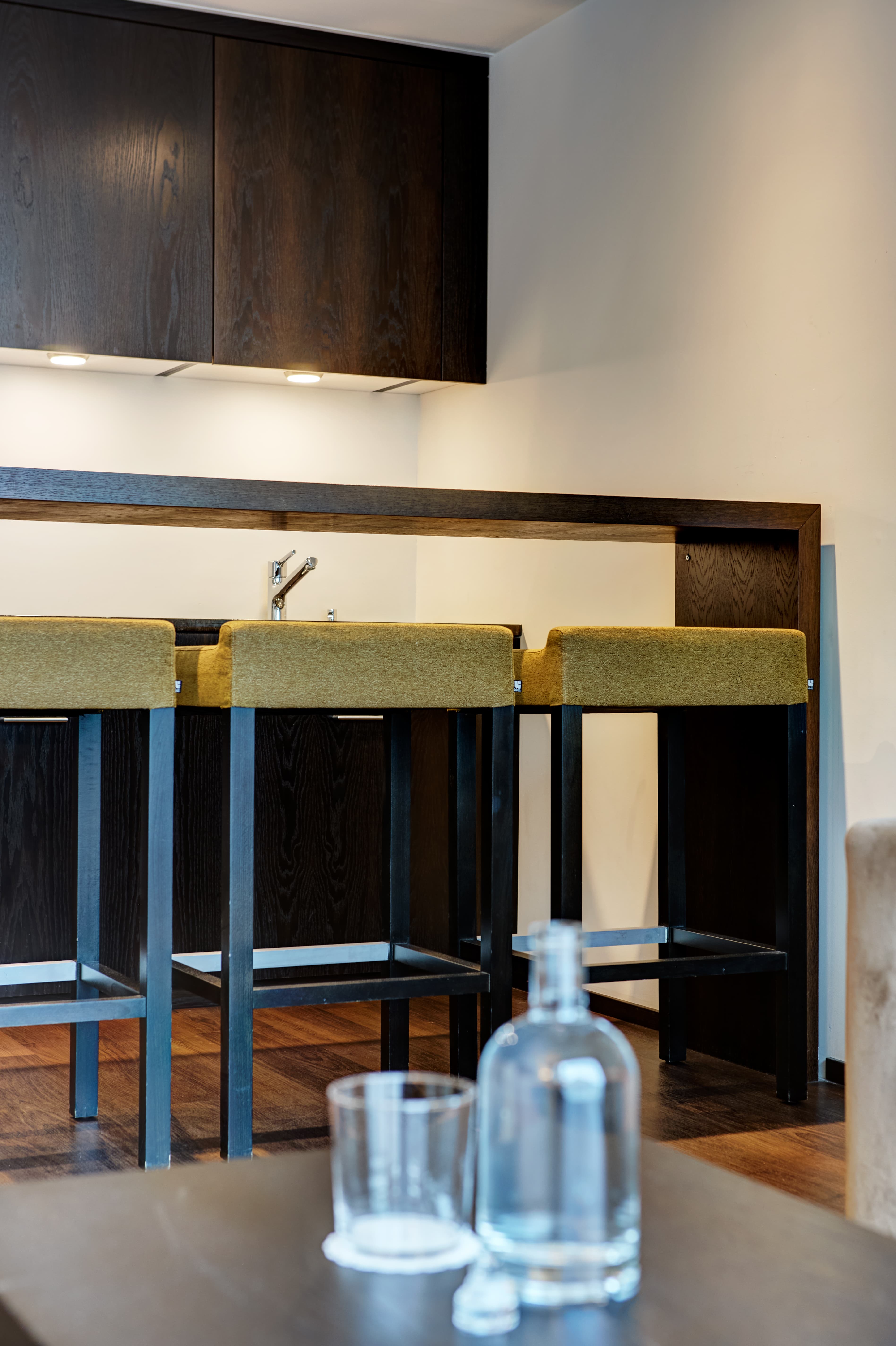 Modern junior suite in the B smart Hotel Widnau with stylish bar stools at a counter and dark wooden furniture.