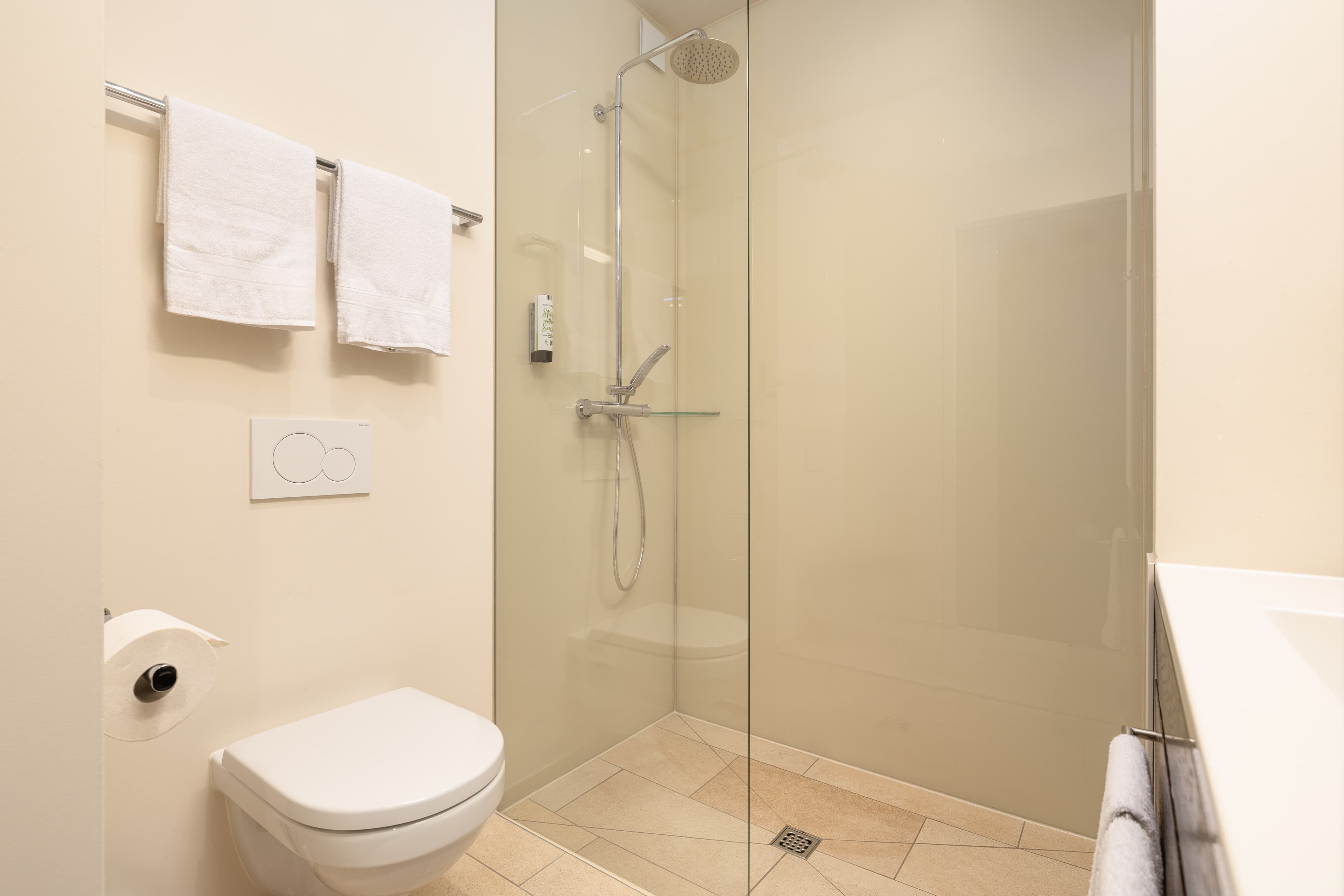 A modern bathroom in the Junior Suite of the B Smart Hotel Widnau with a toilet, glass door shower, and white towels on the wall