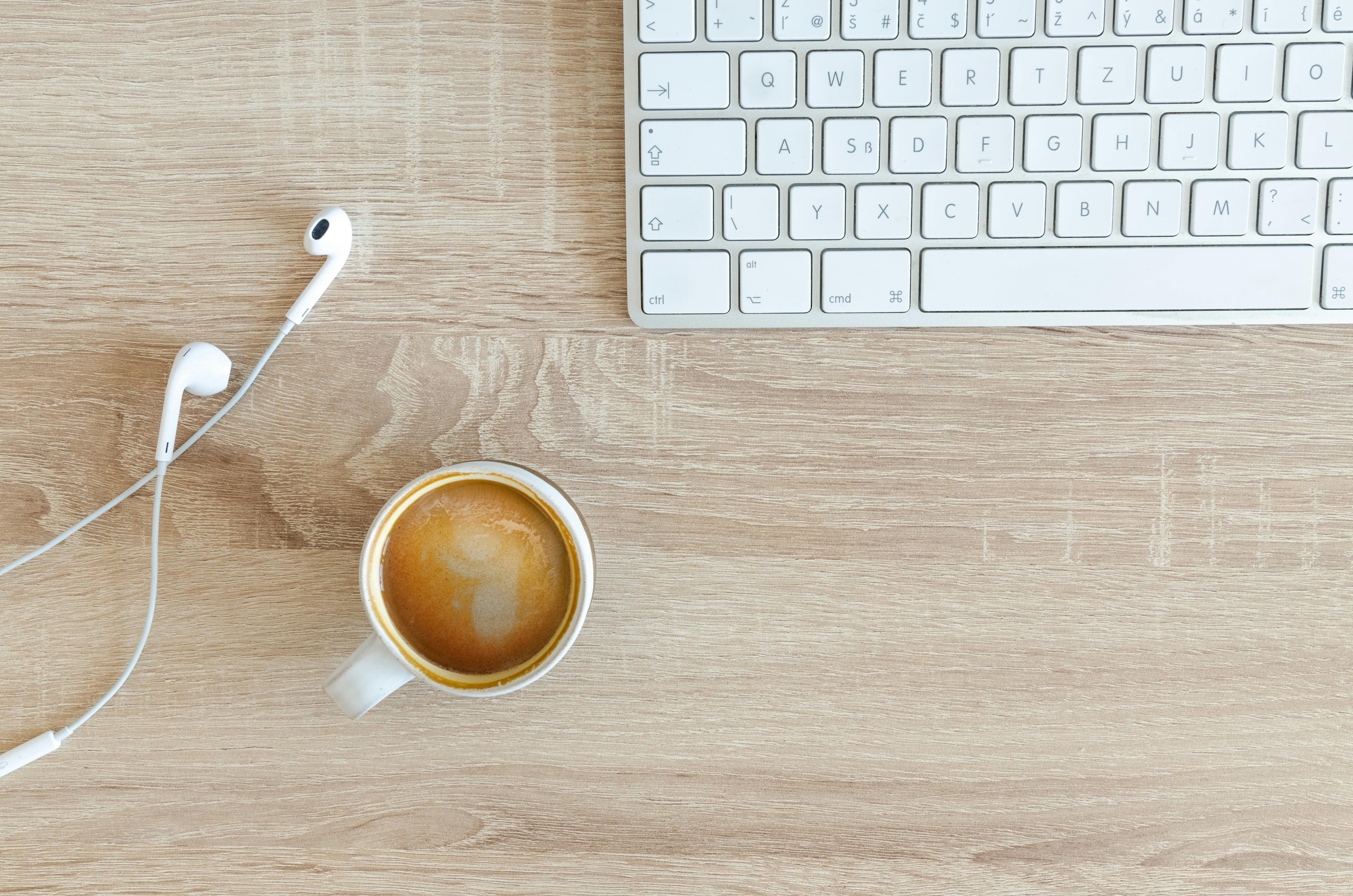 A coffee mug white headphones and a computer keyboard on a wooden table