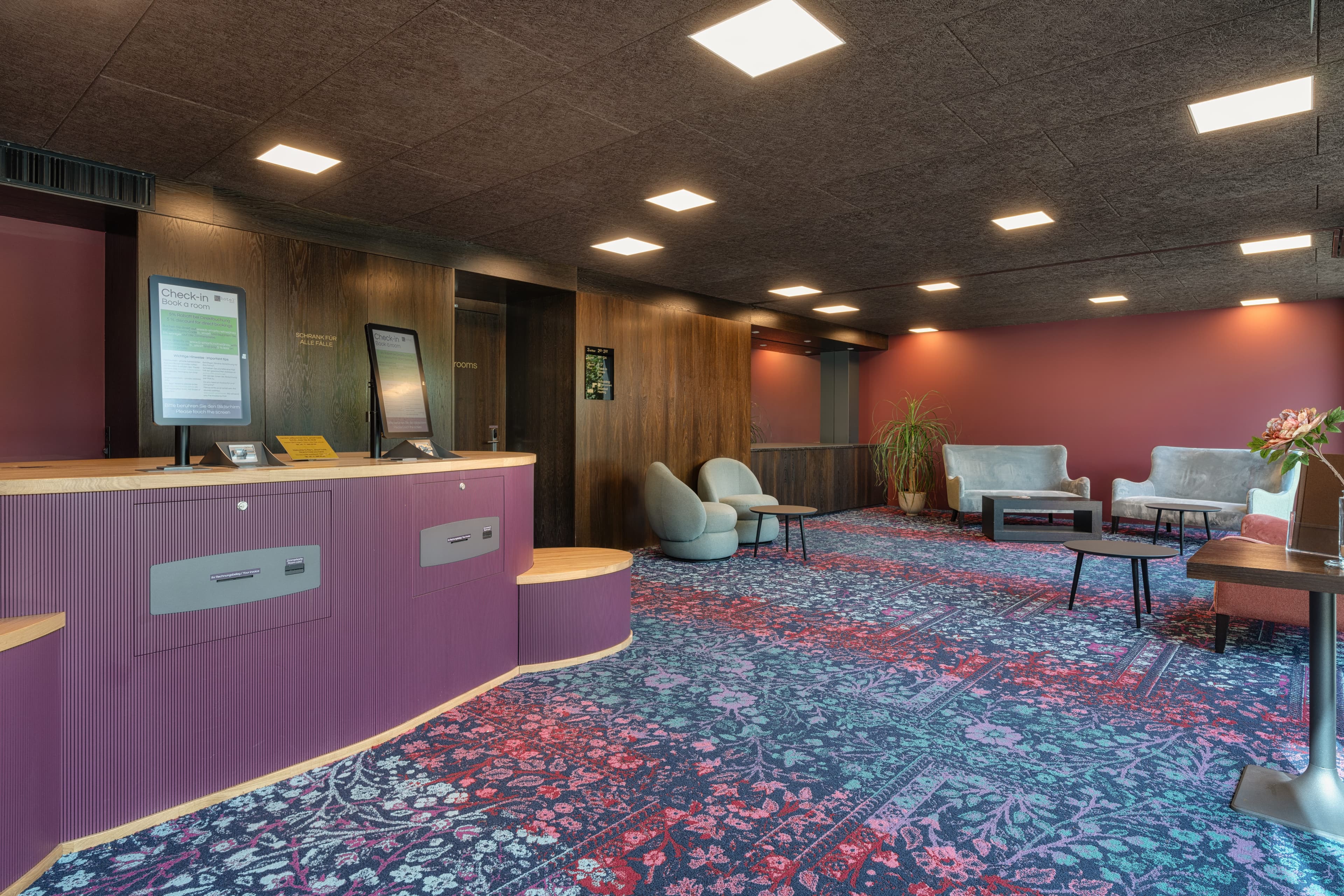 Reception area in the b_smart Hotel Widnau with self check-in counter, modern seating furniture, and floral carpet.